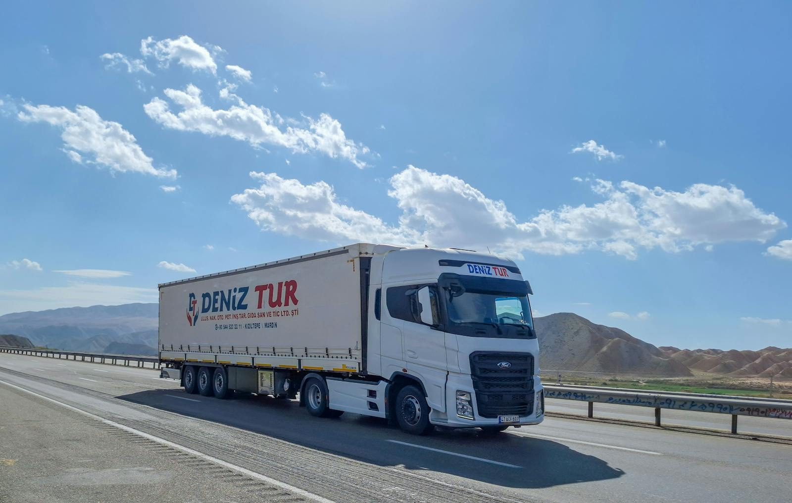 A Deniz Tur truck travels on a sunny highway in Tabriz, Iran, showcasing logistics on the road.